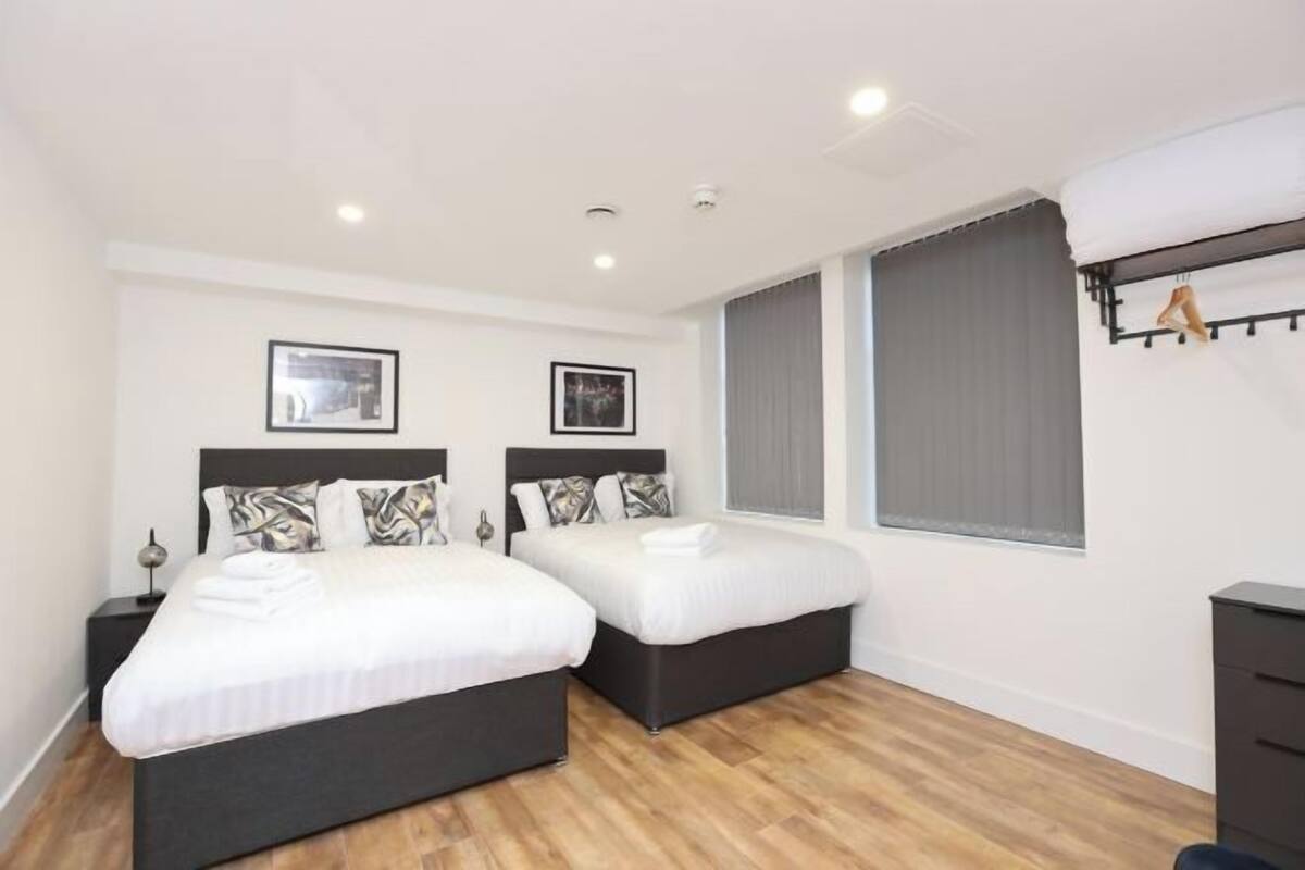 Habitación de hotel con dos camas, un escritorio y un ventanal grande con cortinas.