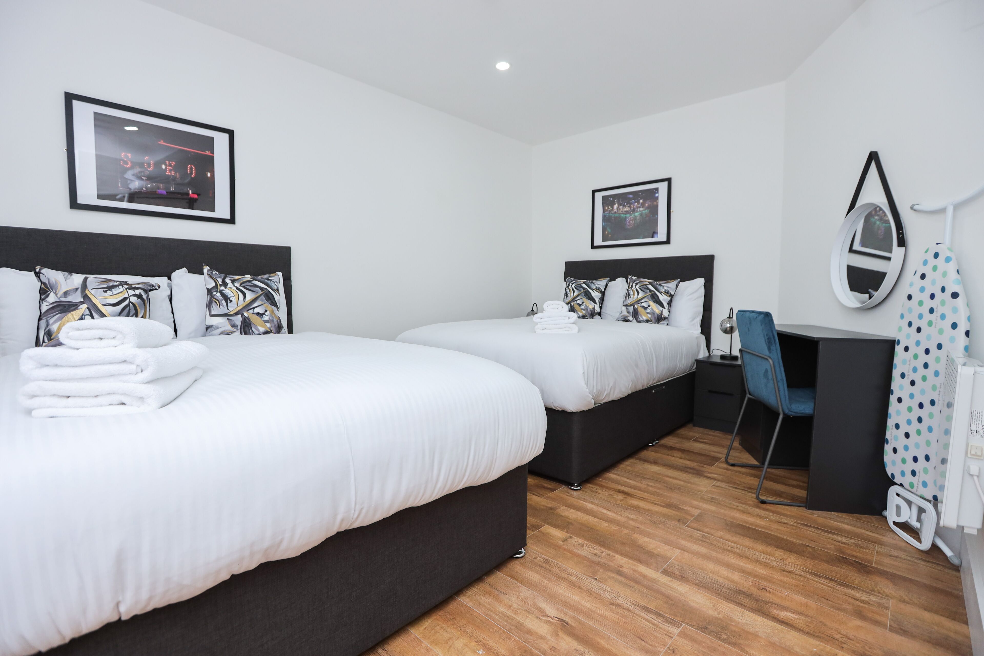 Una habitación de hotel moderna con dos camas, un escritorio, una silla, un espejo y un cuadro en la pared.
