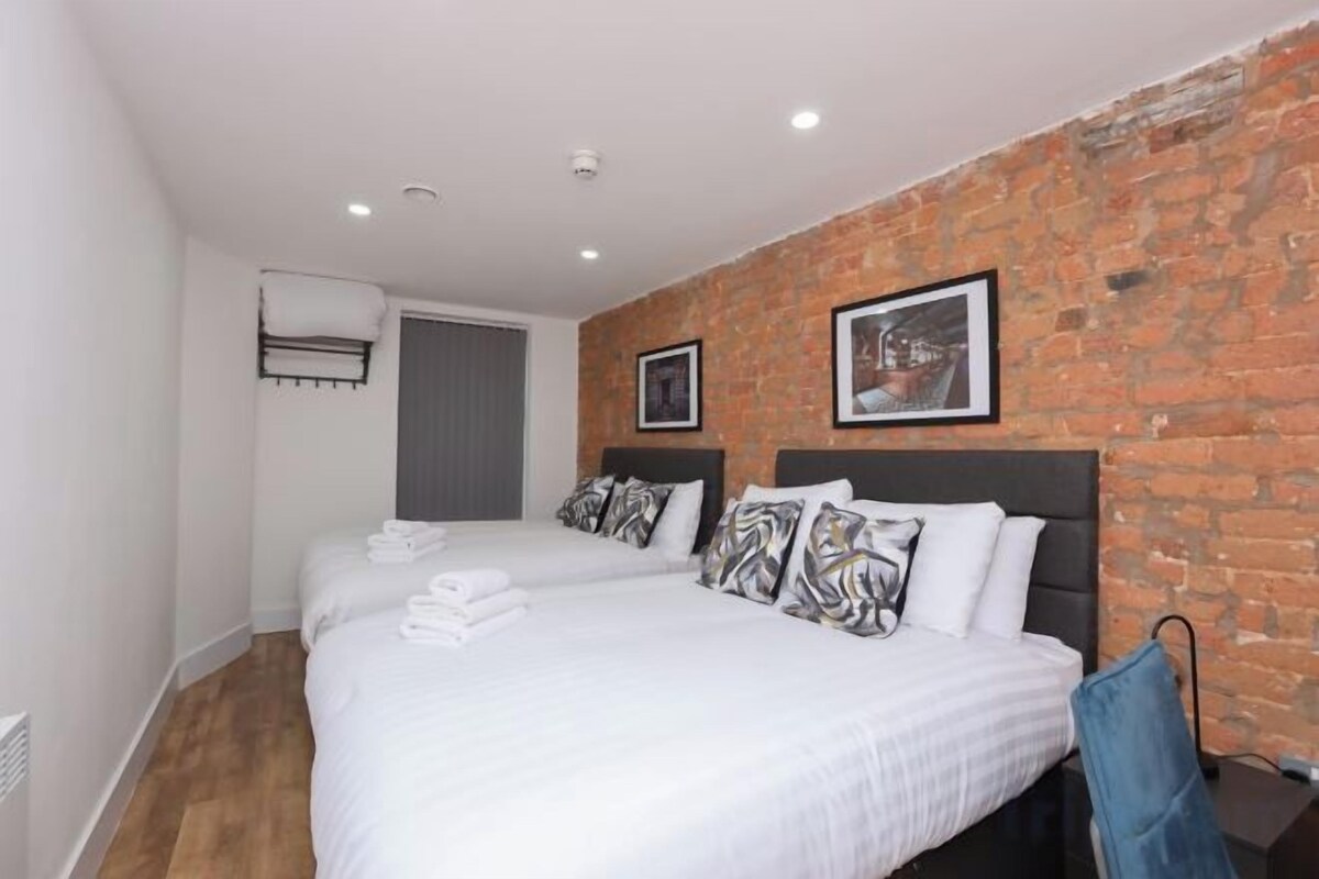 A hotel room with two beds, a brick wall, and a framed picture.