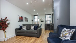 A modern living room with a grey sofa, a blue armchair, and a wooden floor. - Wood Street Apartments (Liverpool)