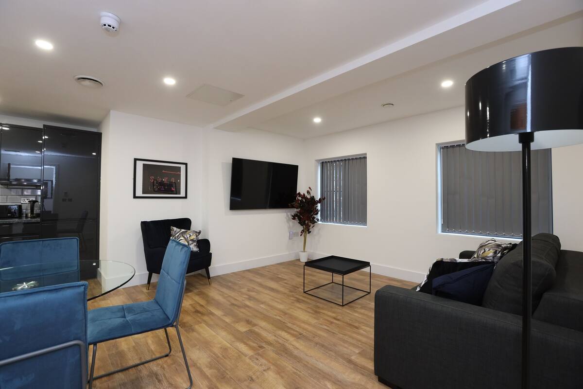 Una sala de estar moderna con un televisor de pantalla plana, un sofá, una mesa de centro y una zona de comedor con una mesa de vidrio y sillas.
