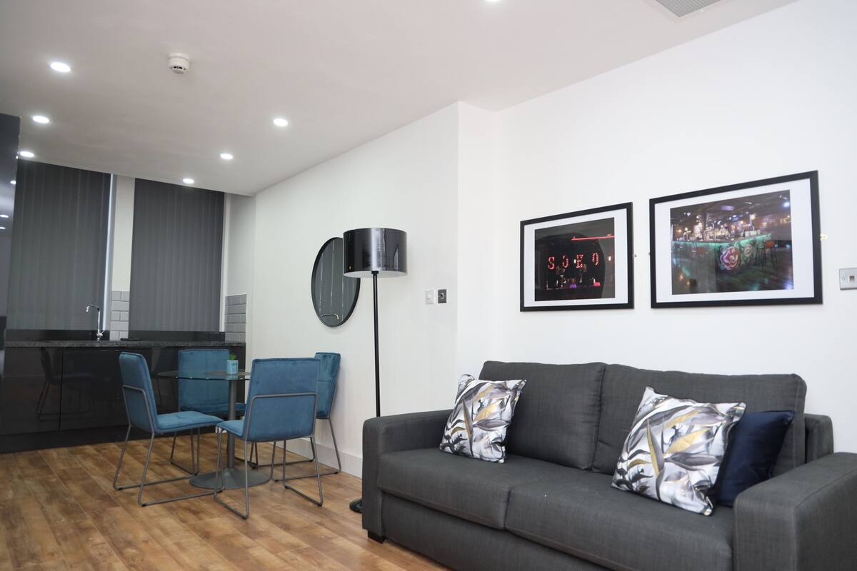 Una sala de estar moderna con un sofá gris, dos sillones azules, una lámpara de pie negra y dos cuadros en la pared.