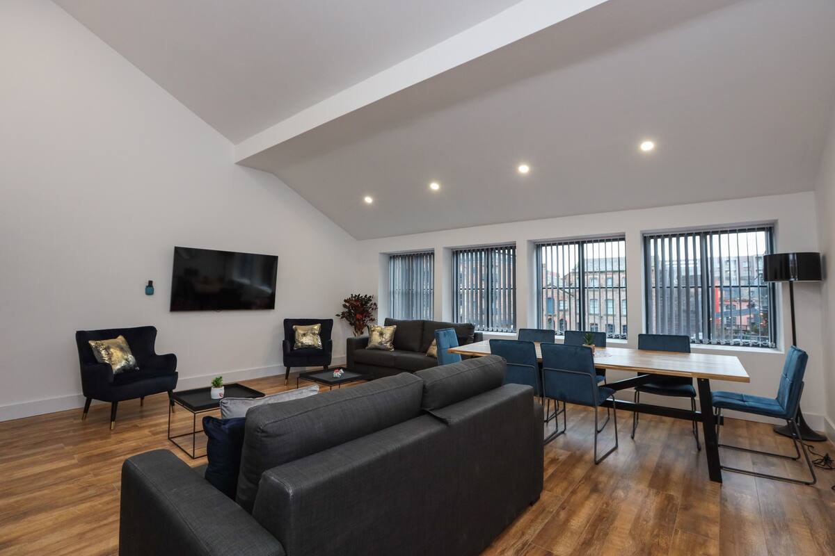 Una sala moderna con un sofá, sillas, una mesa de comedor y un televisor montado en la pared.