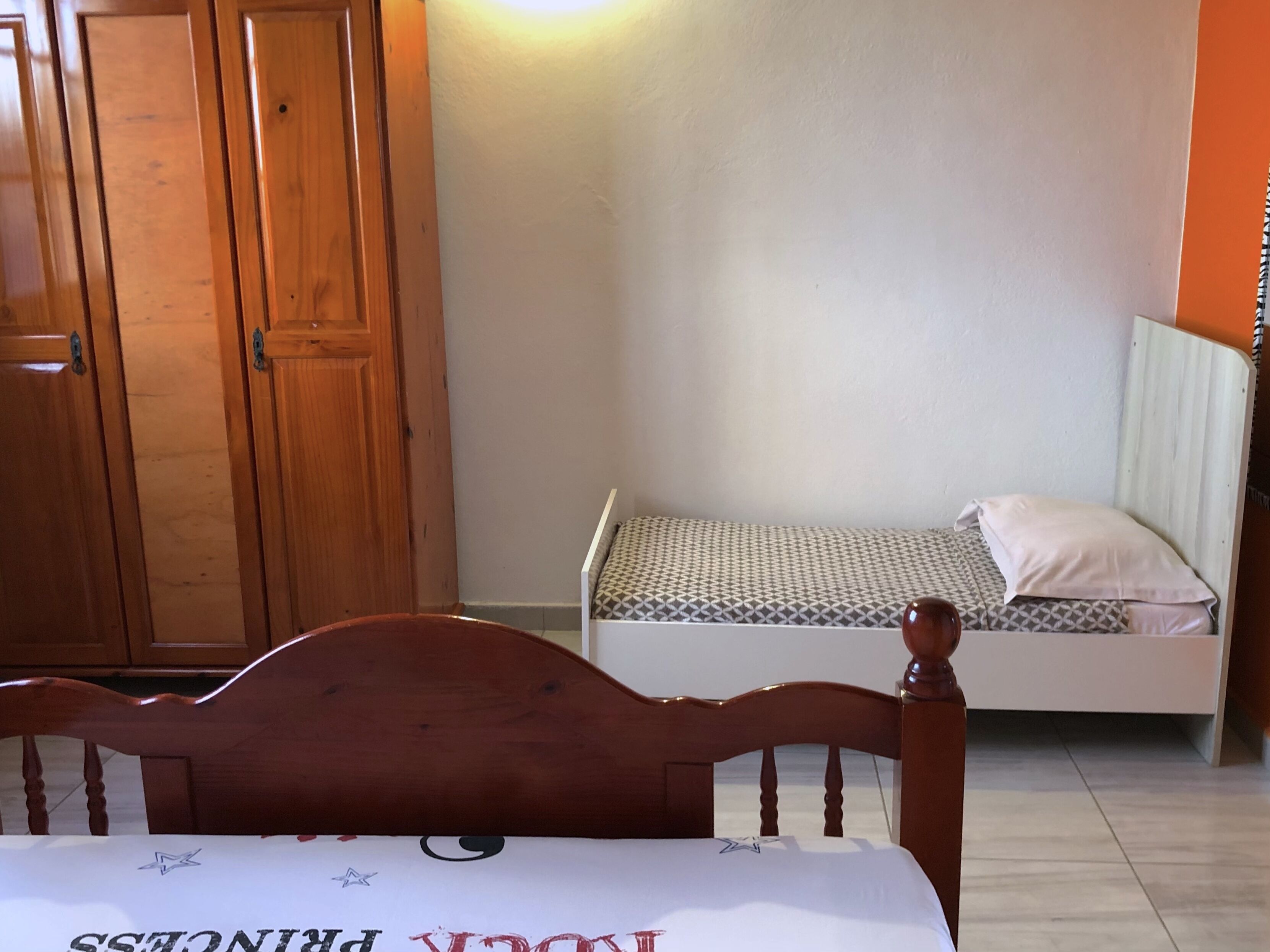 A bedroom with a wooden bed, a small bedside table, a wardrobe, and a mattress on the floor.