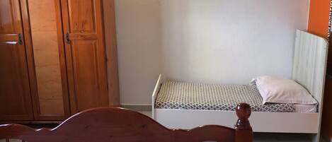 A bedroom with a wooden bed, a small bedside table, a wardrobe, and a mattress on the floor.