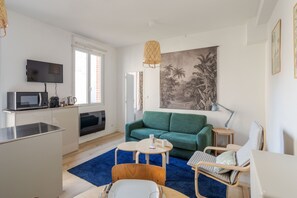 A modern living room with a green sofa, a small round table, and a TV mounted on the wall.