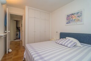 A bedroom with a bed, a wardrobe, a painting, and a laundry area.