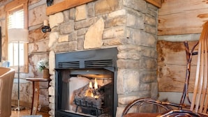 A cozy cabin interior with a stone fireplace, a wooden ceiling, and a patterned rug.