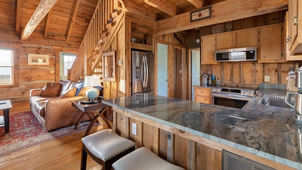 A rustic cabin interior with a wooden ceiling, a large kitchen with modern appliances, a bar area, and a cozy seating space.