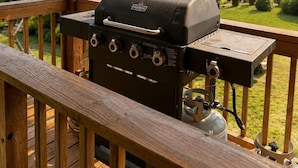 A wooden deck with a barbecue grill and a view of a house and hills in the background.