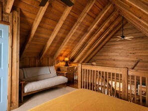 A cozy attic bedroom with a wooden ceiling, a bed, a nightstand, and a ceiling fan.