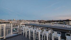 Una terraza en la azotea con sillas blancas y vistas a un paisaje urbano.