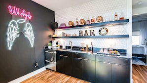 A modern kitchen with a neon sign, wooden flooring, and a bar area with shelves of bottles and glasses. - Rooftop deck, hot tub & neon game room | Nashville, sleeps 12 (Nashville)