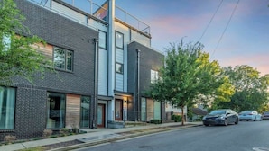 A modern two-story residential building with a brick facade, large windows, and a visible garage. - Rooftop deck, hot tub & neon game room | Nashville, sleeps 12 (Nashville)
