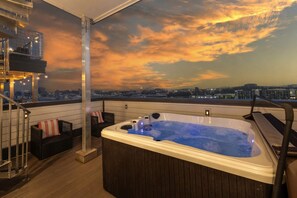 A rooftop terrace with a hot tub, a staircase, and a city view at sunset.