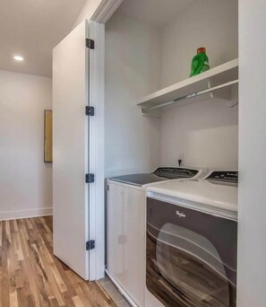 Un cuarto de lavandería con una puerta abatible, una lavadora y un estante con una botella verde.