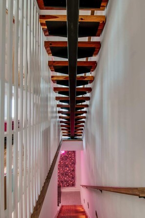 Un pasillo con estructura de techo de madera, paredes blancas y un extremo con pared rosa.
