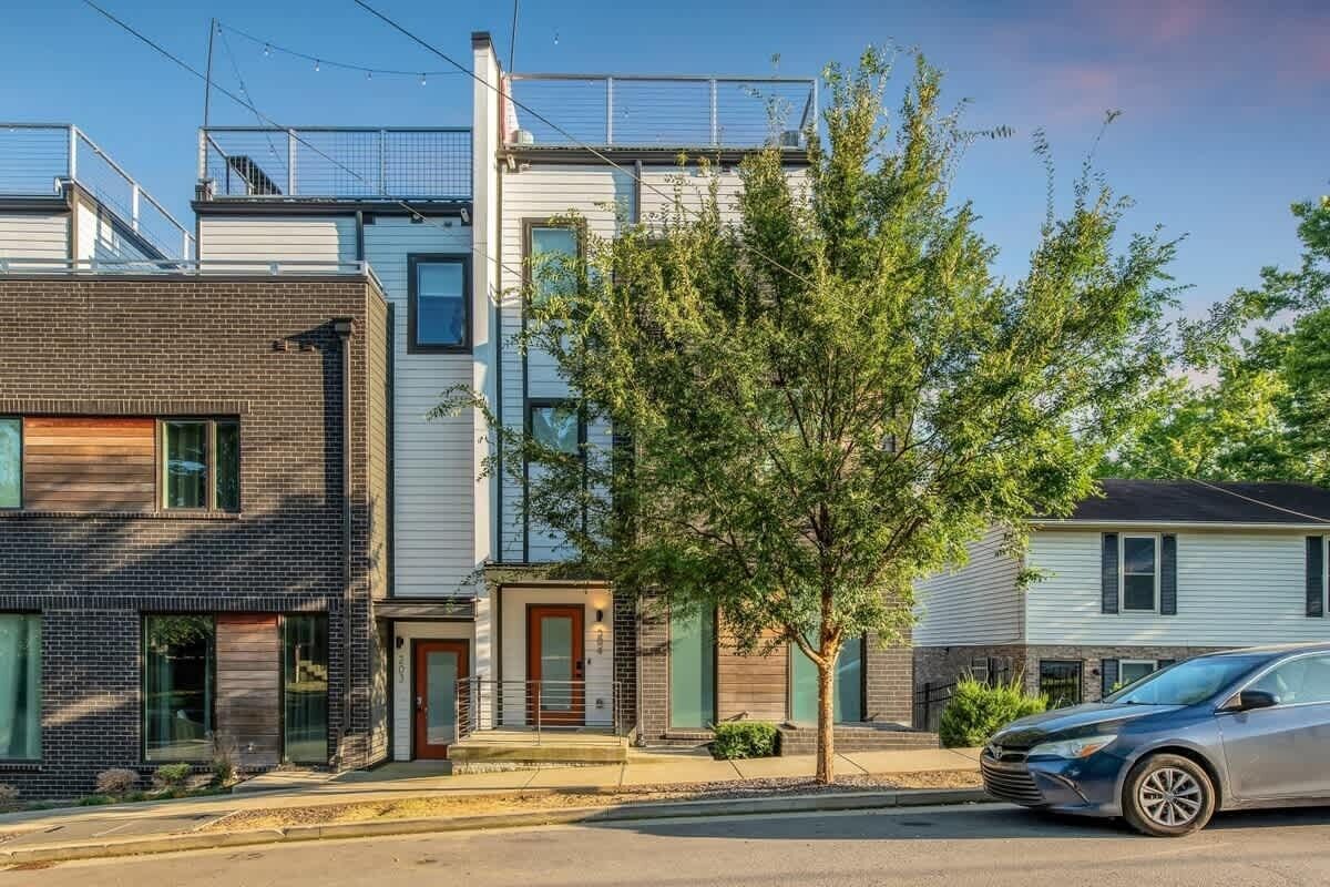 Une rue résidentielle bordée de maisons modernes, avec un arbre au premier plan et une voiture garée.