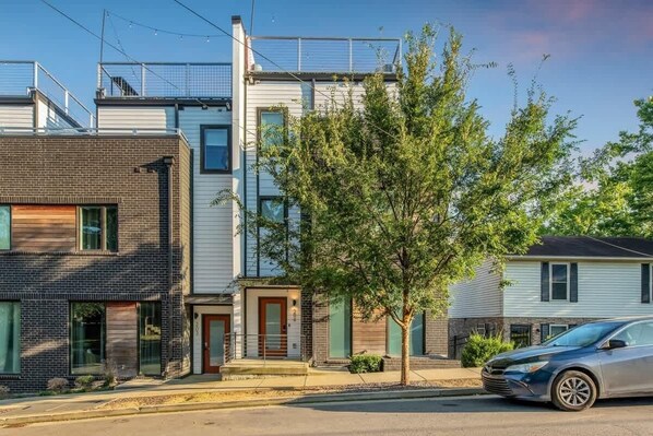 Una calle residencial con casas modernas, un árbol en primer plano y un automóvil estacionado.