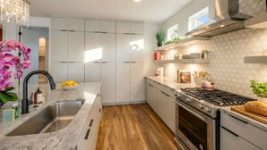 A modern kitchen with white cabinets, a stainless steel sink, a gas stove, and a wooden floor. - Rooftop deck, hot tub & neon game room | Nashville, sleeps 12 (Nashville)