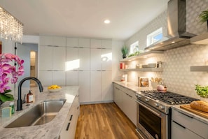 Una cocina moderna con armarios blancos, un lavamanos de acero inoxidable, una estufa a gas y piso de madera.