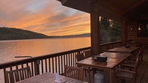 A wooden deck with tables and chairs overlooking a lake at sunset.