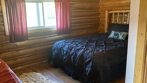 A log cabin bedroom with a bed, a window with curtains, and a wooden floor.