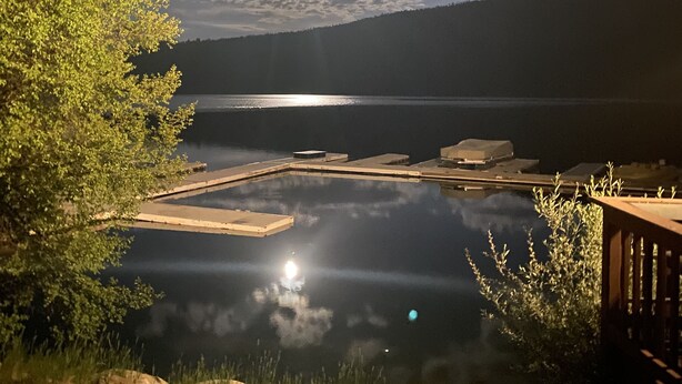 A lakeside view with a wooden dock, calm water, and a clear sky.