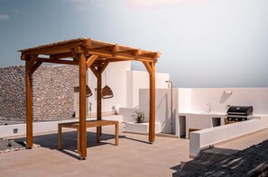 A wooden pergola with a bench, a stone wall, and a modern outdoor kitchen area.