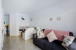 Una sala moderna con un sofá oscuro, una pequeña cocina y una pared blanca decorada.