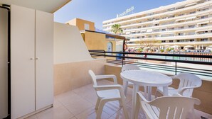 A balcony with white plastic chairs and a table, overlooking a pool area with a hotel building in the background. - Great location!1 bedroom Costa adeje very central (Costa Adeje)