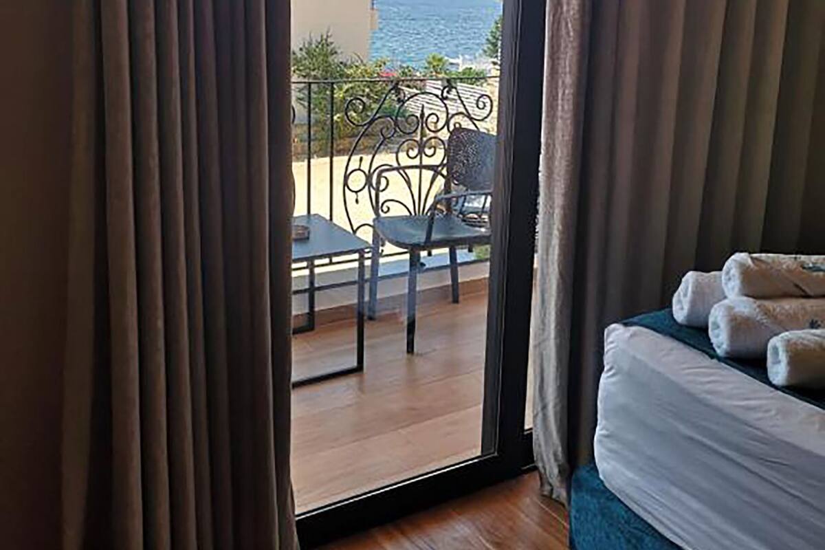 A room with a bed, a view of the sea through a balcony, and a table with chairs outside.