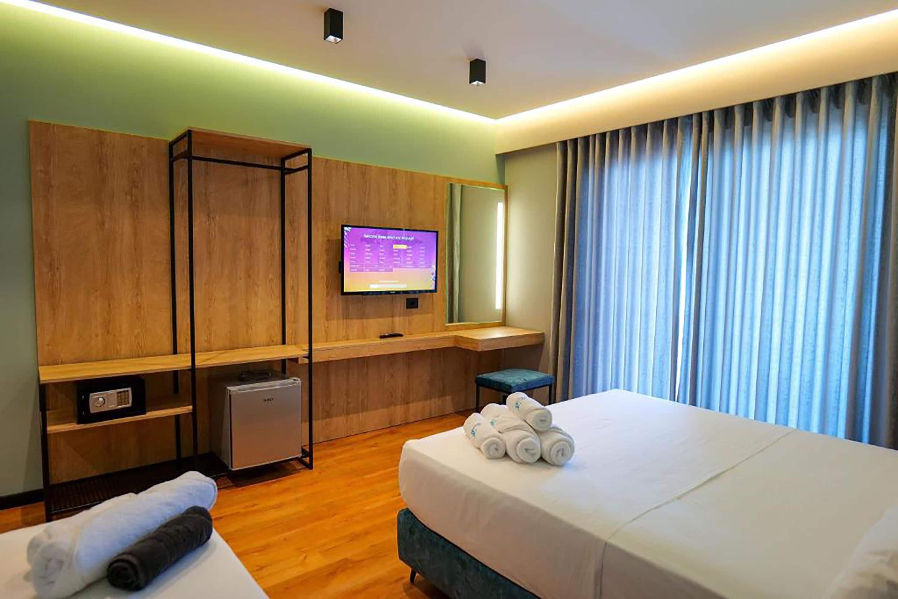 A hotel room with a bed, a TV, a desk, a chair, a small table, and a window with curtains.