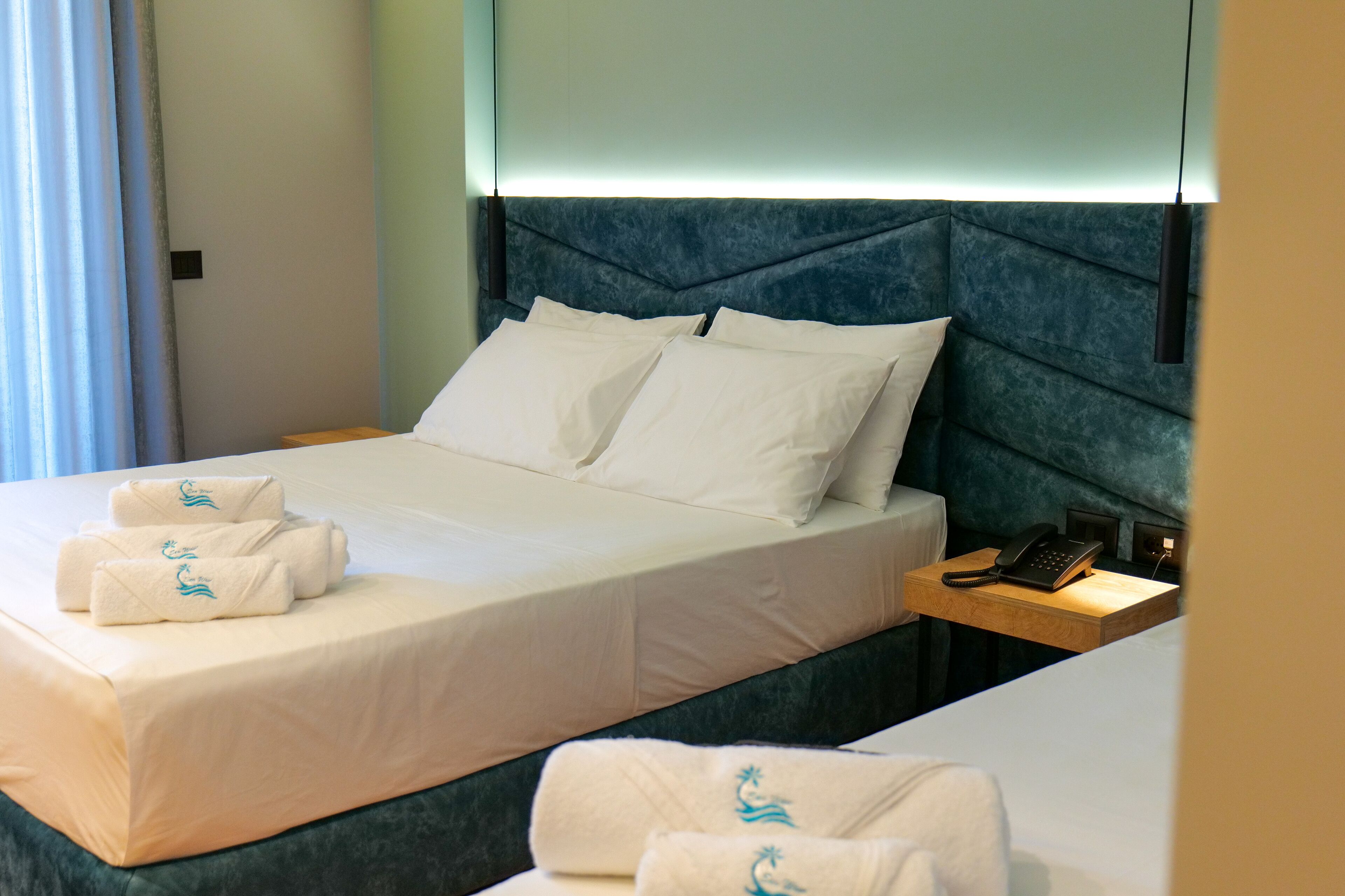 A hotel room with a bed, two pillows, a bedside table with a phone, and towels on the bed.