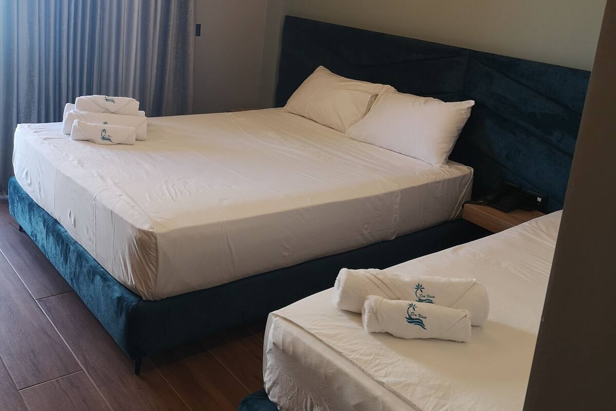 A hotel room with two beds, each with white linens and matching pillows. There is a wooden floor and a blue headboard.