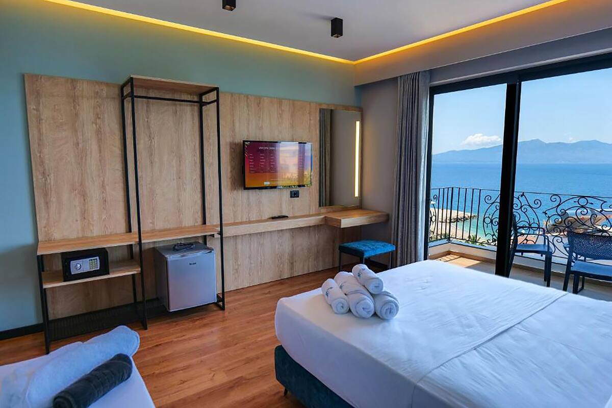 A hotel room with a bed, a TV, a desk, and a balcony with a view of the sea.