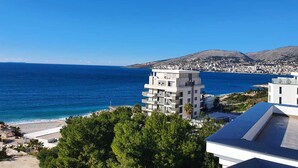 A coastal view with a modern building, clear blue sea, and distant hills. - Seawave Hotel (Sarandë)