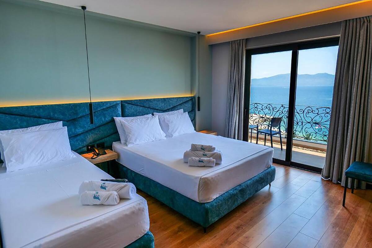 A hotel room with two beds, a view of the sea, and a balcony with a chair.