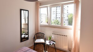 A room with a bed, a chair, a small table with a plant, a radiator, and a window with curtains. - Mary's Apartment (Zagreb)