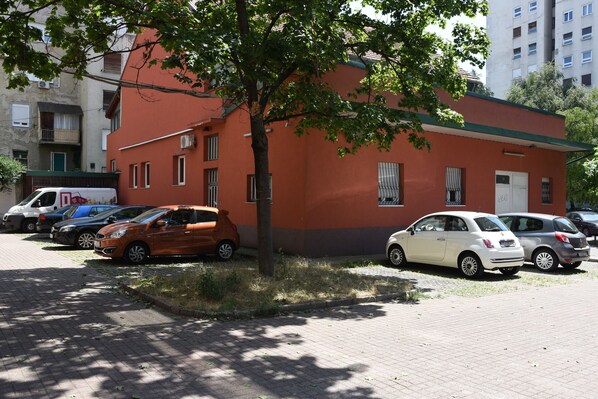 A parking lot with several cars parked in front of a building with a red and grey facade. - Mary's Apartment (Zagreb)