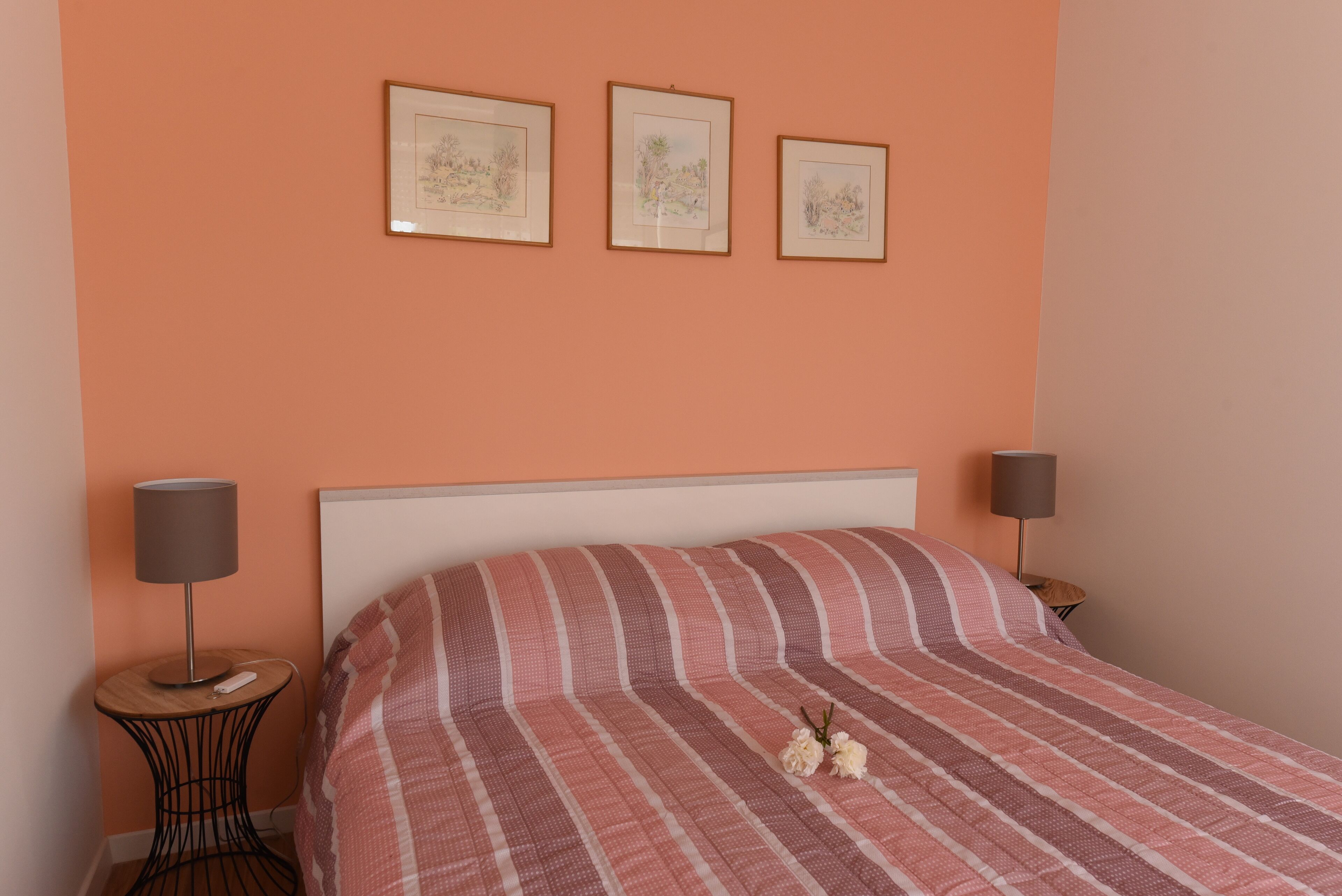 A bedroom with a bed, two bedside tables, and three framed artworks on the wall.