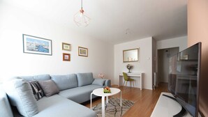 A modern living room with a grey sofa, a white coffee table, and a flat-screen TV on a white stand. - Mary's Apartment (Zagreb)