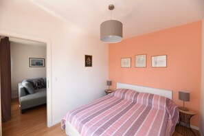 A bedroom with a bed, a nightstand, a lamp, and a sofa in the adjacent room. - Mary's Apartment (Zagreb)