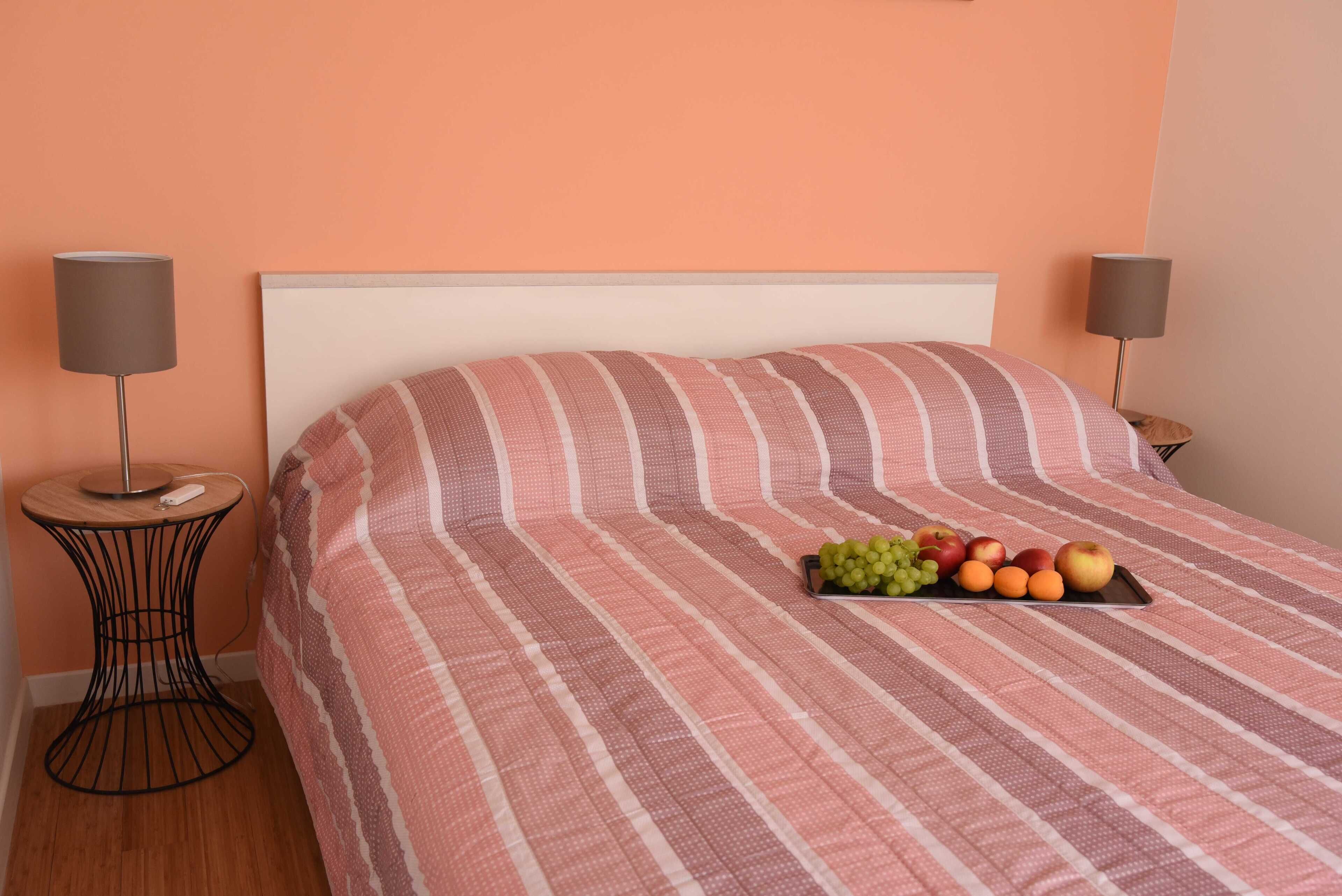 A neatly made bed with a striped bedspread and a tray of fruit on the pillows.