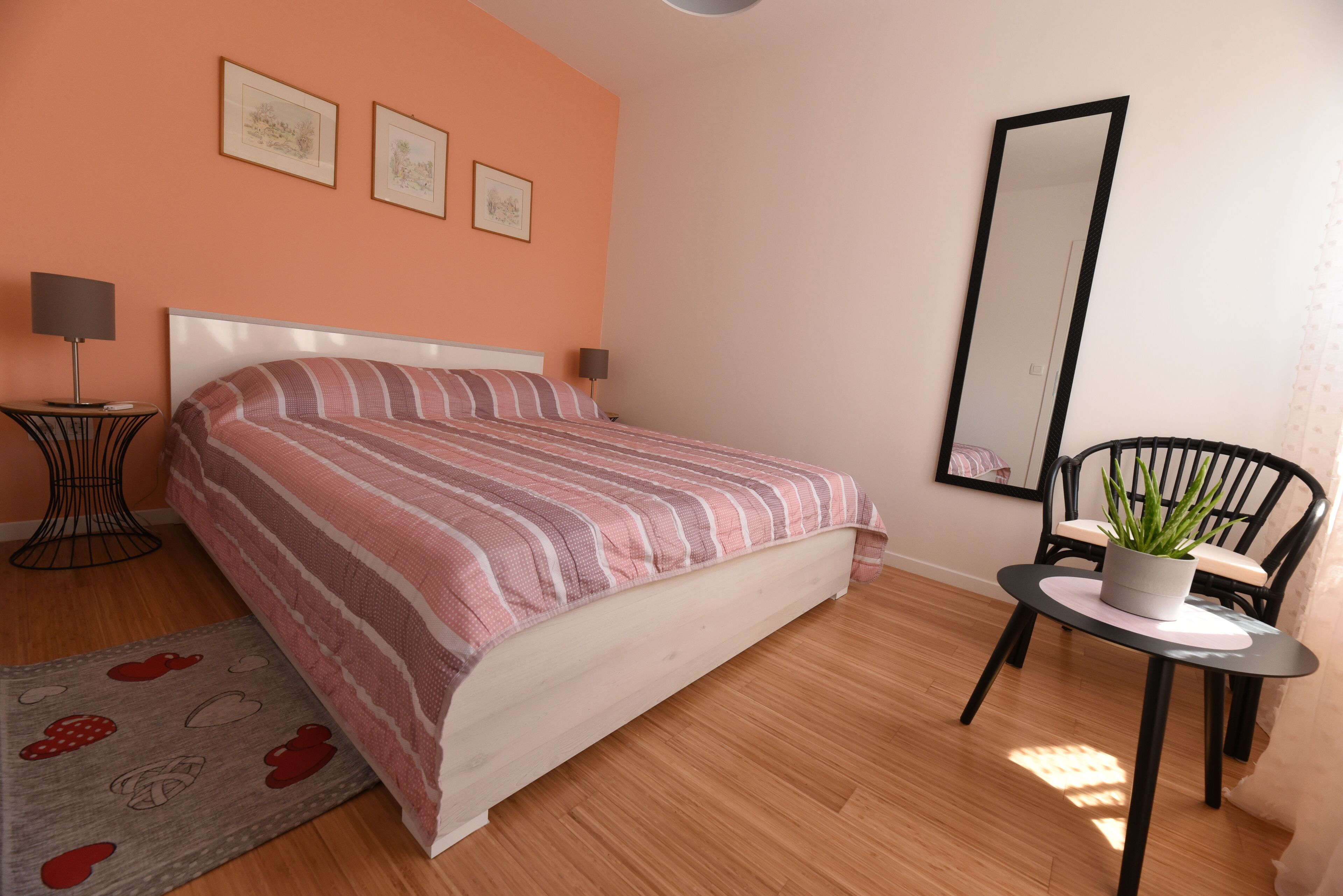 A bedroom with a bed, bedside tables, a chair, a mirror, and a potted plant.
