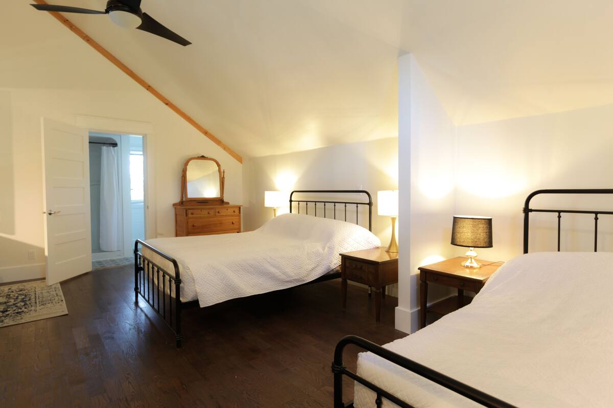 A bedroom with two beds, wooden furniture, a ceiling fan, and a mirror.