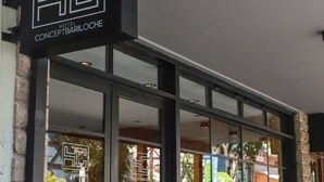 Entrada de hotel con amplias puertas de vidrio, un logotipo visible y vistas a la calle a través de las ventanas.