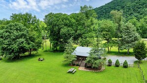 Eine Hütte mit einer kleinen Terrasse, umgeben von üppigem Grün und einer Hügelkulisse im Hintergrund.