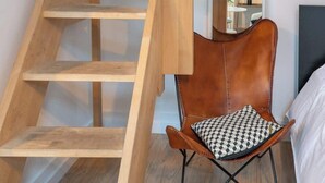 A modern interior with a wooden staircase, a leather chair with a patterned cushion, and a bed with white bedding. - Amazing studio located in Ghent (Gent)