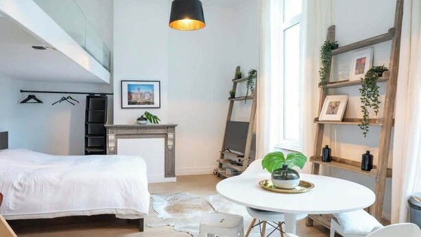 A modern bedroom with a bed, a round dining table with chairs, a fireplace, and a large window. - Amazing studio located in Ghent (Gent)